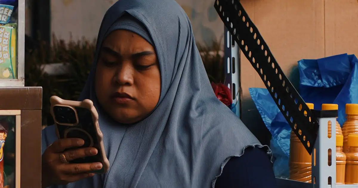 Perempuan berjilbab di warungnya menatap layar ponsel
