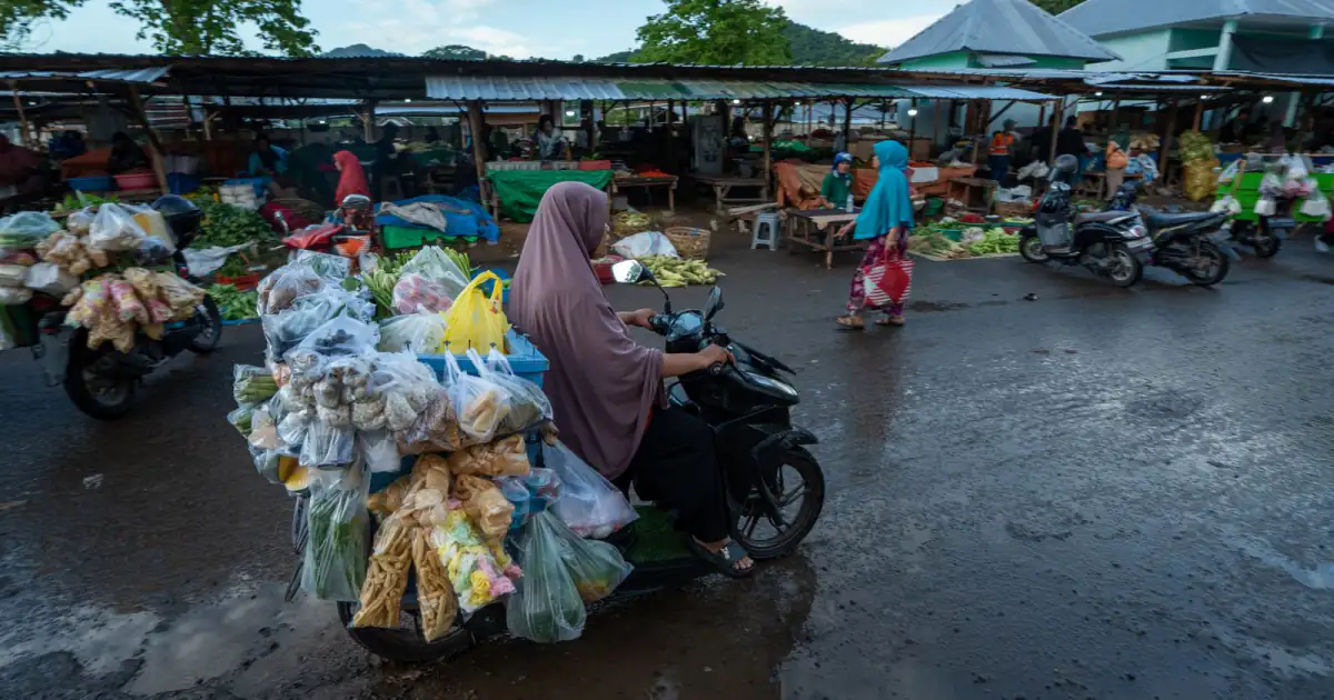 Perempuan mengendarai motor penuh muatan dagangan melintasi pasar