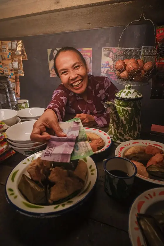 Pemilik warung tersenyum menerima pembayaran dari pembeli